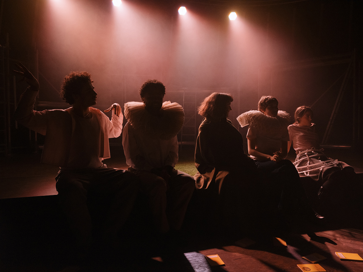 Vier Schauspielende, die auf der Bühne sitzen